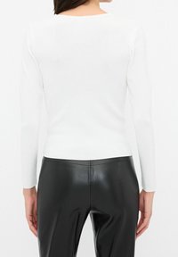 Haut blanc à manches longues avec un col rond dégagé, en tissu côtelé, associé à un pantalon noir ajusté avec une finition lisse.