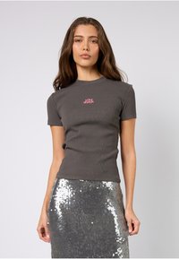 Szary prążkowany t-shirt z krótkim rękawem z różowym napisem "LOVE SEASON" na piersi, zestawiony z błyszczącą, srebrną spódnicą pokrytą cekinami.