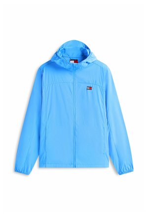 Coupe-vent à capuche bleu clair avec fermeture éclair frontale et petit logo rectangulaire rouge, blanc et bleu sur la poitrine gauche.