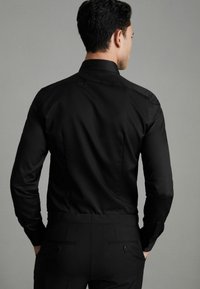 Cămașă neagră cu nasturi, cu mâneci lungi, dintr-un material neted, cu un design ajustat și o guler clasic. Croiala adaptată scoate în evidență silueta.