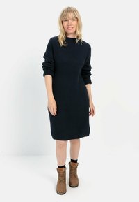 Navy-blaues, geripptes Strickkleid mit langen Ärmeln, lockerer Passform und Rundhalsausschnitt. Kombiniert mit braunen Schnürstiefeln, die eine strukturierte Oberfläche aufweisen.