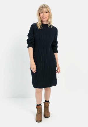 Navy-blaues, geripptes Strickkleid mit langen Ärmeln, lockerer Passform und Rundhalsausschnitt. Kombiniert mit braunen Schnürstiefeln, die eine strukturierte Oberfläche aufweisen.