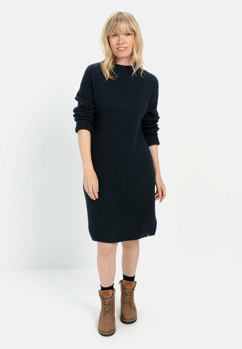 Navy-blaues, geripptes Strickkleid mit langen Ärmeln, lockerer Passform und Rundhalsausschnitt. Kombiniert mit braunen Schnürstiefeln, die eine strukturierte Oberfläche aufweisen.
