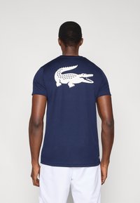 Granatowy t-shirt z krótkim rękawem wykonany z gładkiej tkaniny, z dużym białym nadrukiem krokodyla na plecach. Minimalistyczny design i dopasowany krój.