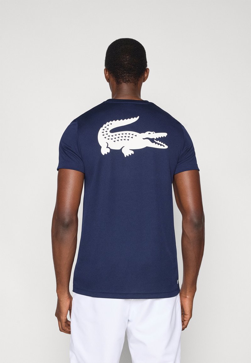 Granatowy t-shirt z krótkim rękawem wykonany z gładkiej tkaniny, z dużym białym nadrukiem krokodyla na plecach. Minimalistyczny design i dopasowany krój.