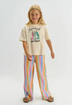 Krémové tričko s grafikou "Mermaid OFF DUTY". Pruhované nohavice s širokými nohavicami v pastelových farbách. Sandále s plochou podrážkou a s detailom na pracku.