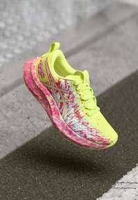 Leichtgewichtigem gelben Sportschuh mit pinken und blauen Mustern, Mesh-Obermaterial, gepolstertem Sohlen und erhöhten Akzenten. Ideal für Leistung und Komfort.
