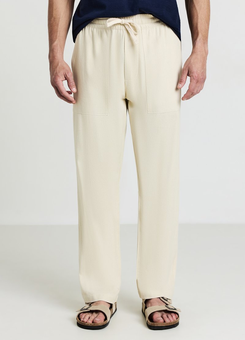 Pantaloni beige chiaro, dalla vestibilità ampia, con elastico in vita, tasche applicate frontali e una texture di tessuto liscia e leggera.