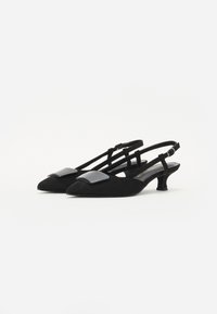 Zapatos de slingback de ante negro con punta afilada, que presentan un acento negro brillante en la parte frontal y un tacón pequeño y grueso.