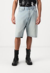Pantalones cortos de mezclilla azul claro con un ajuste relajado, bolsillos frontales y un ligero desvanecimiento, combinados con botines negros de cuero.