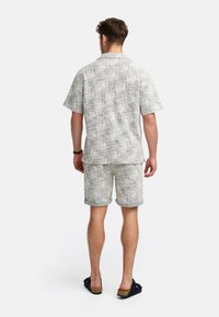 Kurzarmhemd und passende Shorts aus einem hellgrauen Stoff mit einem dezenten strukturierten Muster und umgeschlagenen Säumen. Offenes Kragen-Design.