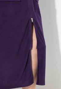 Fialová sukně vyrobená z měkké látky s bočním zipem a vysokým rozparkem, která vykazuje jednoduchý, ležérní design.