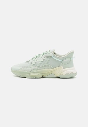 Jasnozielony mesh i skórzany sneaker z falistą podeszwą, sznurowaniem z przodu i wyściełanym kołnierzem, pokazany z profilu na białym tle.