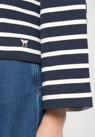 Men's navy and white striped long-sleeve shirt with a round collar, featuring an embroidered bee logo on the left hem, paired with blue denim.