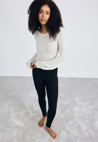 Creme lange mouw top gecombineerd met zwarte leggings. De top heeft een ronde halslijn en aansluitende mouwen, terwijl de leggings strak om het lichaam vallen.