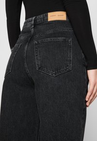 Svarta denimjeans med en något blekt textur, med hög midja, stora bakfickor och en läderlogotyp på midjebandet.