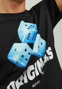 Svart t-shirt med en grafisk design av tre blå tärningar som visar vita prickar, samt fet vit text som säger "ORIGINALS" och "INIT FOR ME."