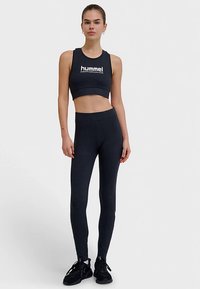 Haut court de sport noir avec logo blanc, associé à des leggings noirs taille haute. Texture lisse, design ajusté, adapté pour la pratique sportive.