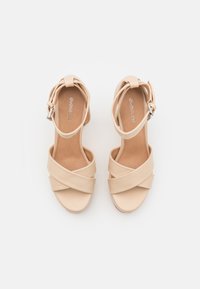 Beżowe sandały na wysokim obcasie z krzyżującymi się paskami, klamrą wokół kostki, gładkim materiałem ze sztucznej skóry i zaokrąglonym noskiem.