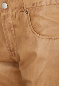 Tan leren stof met een gladde textuur, voorzien van een voorkantzak, stiksels aan de bovenkant en een zilveren drukknoopdetail.