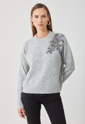 Grå strikket genser med avslappet passform, rund hals og dekorativ blomsterdesign på venstre skulder. Teksturert, myk stoff.