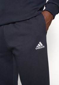Pantalones deportivos color navy en material suave con corte ajustado. Presenta un logotipo de Adidas bordado en blanco en el muslo izquierdo.