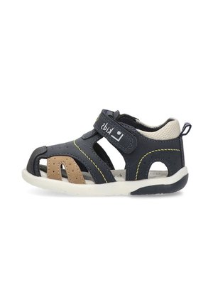 Sandalia para niño pequeño en azul navy y beige con tira de Velcro, punta abierta, suela blanca acolchada y cuello de talón de malla transpirable.