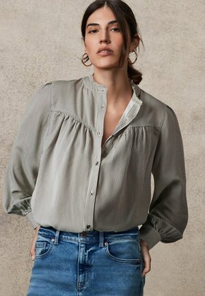 Gestreepte blouse met een hoge halslijn, knoopsluiting aan de voorkant en geplooide details bij de schouders, gedragen met blauwe high-waisted denim jeans.