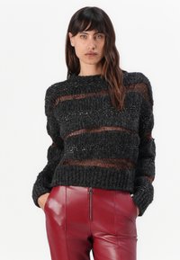 Chunky black knit sweater with horizontal metallic copper stripes, featuring a wide neckline and oversized sleeves, paired with red leather pants.
