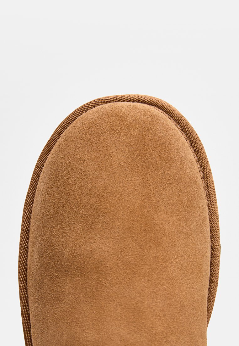 Stivale in suede beige con punta rotonda, caratterizzato da una cucitura in tessuto testurizzato. La forma complessiva è alta fino alla caviglia con una suola flessibile.