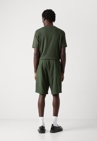 Grøn bomulds T-shirt og shorts sæt, elastisk talje, enkelt design, båret med hvide sokker og sorte sko, vist fra bagsiden.