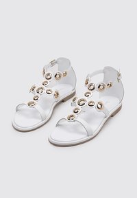 Sandalias blancas de punta abierta con suela plana, que presentan acentos circulares dorados y un cierre de hebilla en el tobillo. Material duradero y diseño minimalista.
