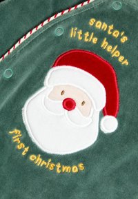 Tessuto in pile verde con un volto di Babbo Natale ricamato, dotato di un cappello rosso, barba bianca e la scritta: "il piccolo aiutante di Babbo Natale" e "primo Natale."