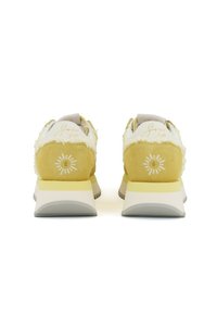 Zapatillas deportivas en amarillo y blanco, con un acolchado en la parte trasera, diseño elegante, suela gris y detalle gráfico del sol en el talón.