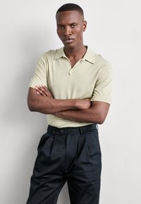 Lys grønn kortermet polo skjorte med hakkekrage, kombinert med høyt liv svarte bukser med frontfold og knappelukking.