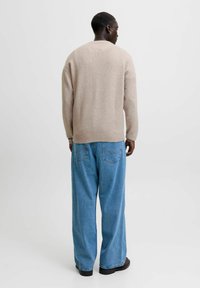 Beige stickad tröja med ribbade manschetter och fåll, i kombination med lösa, ljusblå denimjeans med bakfickor. Svarta skor är synliga.