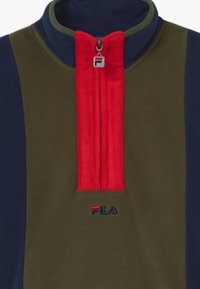 Pullover in pile di colore verde oliva, blu navy e rosso. Presenta un colletto alto, un'apertura con zip a quarti e un logo ricamato all'orlo.