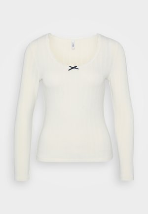 White long-sleeve top with ribbed texture, scoop neck, lace trim, and a black bow accent at the center front. Cotton blend material.