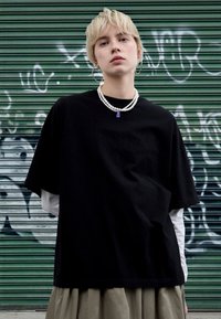 Black oversized t-shirt made of cotton, layered over a white long-sleeve shirt. Accessorized with layered pearl necklaces and hoop earrings.