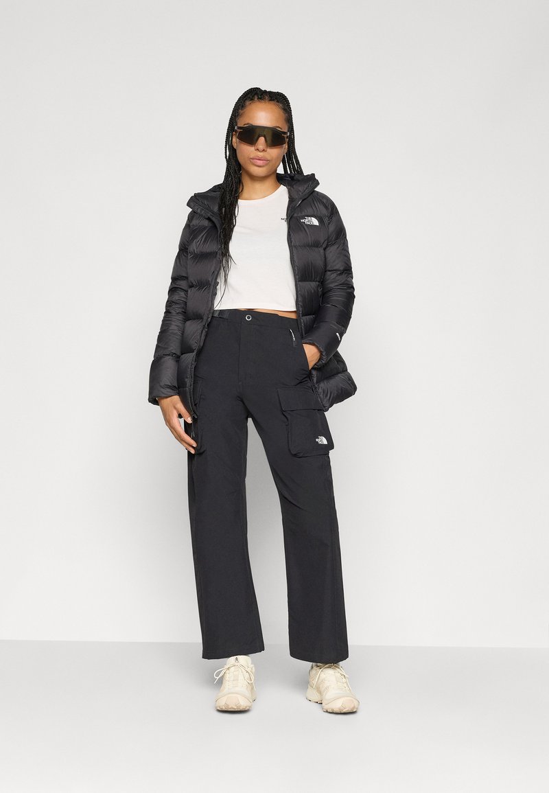 Sort pufferjakke, hvid crop top og sorte cargo-bukser. Flettet hår og oversized sorte solbriller. Lyse sneakers.