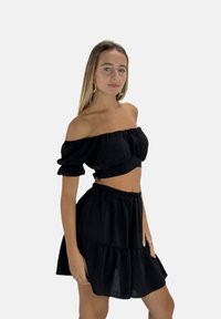 Zwarte off-shoulder cropped top met ruches aan de mouwen en bijpassende gelaagde rok. Zachte stof met een gladde textuur. Elastische tailleband aan de rok.
