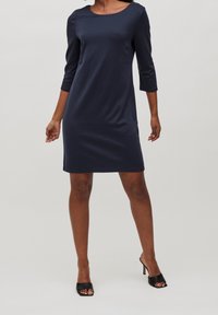 Robe bleu marine avec un col rond, des manches trois-quarts, et une coupe ajustée. Confectionnée dans un tissu doux, elle arrive au-dessus du genou.