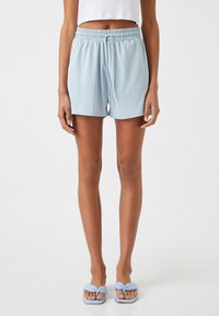 Shorts elásticos de cintura en azul claro con cordón, hechos de una tela suave. Combinados con sandalias planas azules a juego.