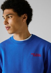Blauw sweatshirt met ribgebreide ronde hals. Bevat rode "RED BULL RACING" tekst op de linkerkant van de borst. Soepele stoftextuur, casual pasvorm.