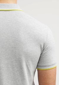 Grå polo t-shirt med korta ärmar, med en kontrasterande gul krage och ribbad halsringning. Tyget har en texturerad, bekv äm framtoning.