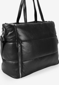Bolso tote de cuero negro con un diseño acolchado. Presenta dos asas resistentes y una cremallera visible que acentúa el lateral. Textura suave.