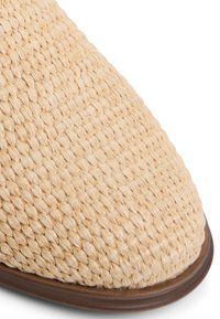 Woven straw shoe in light beige with a pointed toe. Features a smooth brown sole. Texture appears natural and breathable.