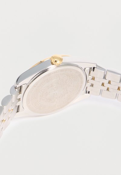 Ασημένιο και χρυσό ρολόι χειρός που δείχνει το χαραγμένο κεφάλι της Μέδουσας στην ανοξείδωτη πίσω πλευρά και τη χρυσή κορόνα στο πλάι.