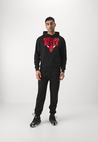 Sort hættetrøje og bukser med det røde "Chicago Bulls" logo og grafik. Materialet ser blødt ud; hættetrøjen har en frontlomme og ribbede manchetter.