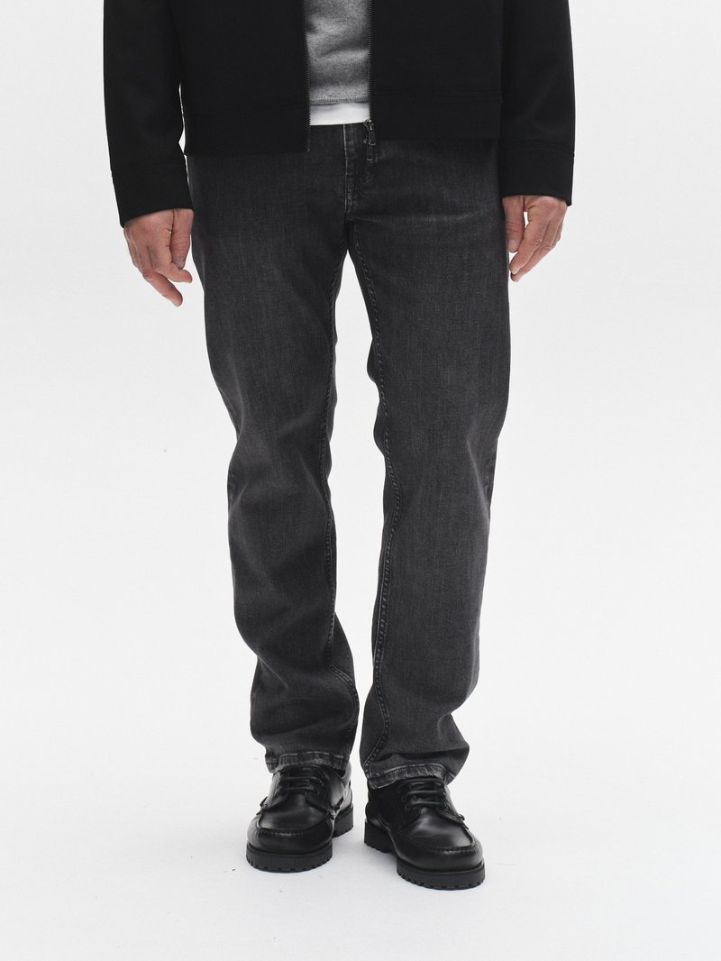 Tamsiai pilkos spalvos džinsai tiesaus kirpimo, derinami su juodais odiniais batais ir juoda užtrauktuku užsegama striuke ant pilkos spalvos džemperio.